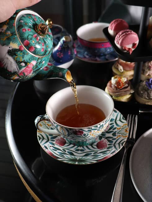 Tea being poured into tea cup with a floral design.