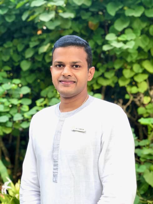 Our wellness expert, Dr. Arun Tomson smiling against a leafy green backdrop
