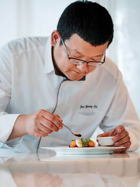 Executive Chef Jaeyoung Lee holds spoon over plate, garnishes small egg dish