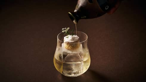 Cocktail topped with a miniture dessert atop a square ice cube