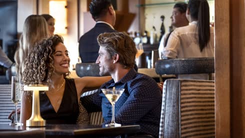 A group of people around a bar and sitting at a table conversing.