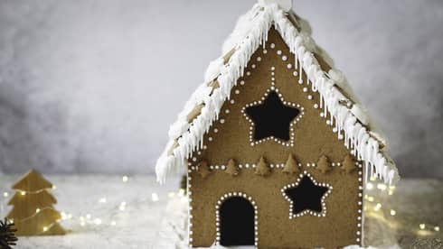 Gingerbread house decorated with white icing amid white background and white lights