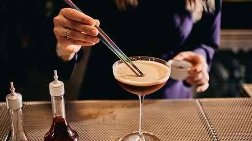 Person standing near a table and stirring a drink in a martini glass