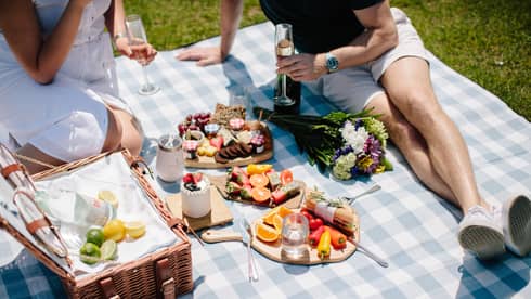Two people enjoying a large picnic in a park during a sunny day.