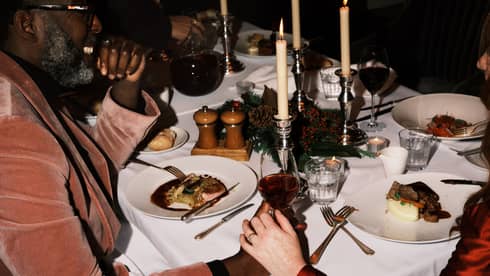 Two guests sitting at a dining table holding hands and a glass of wine.