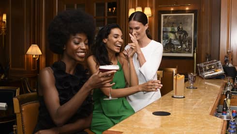 Three girlfriends having drinks and laughing at a hotel bar
