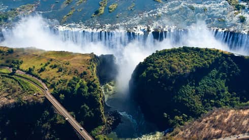 An aerial view of Victoria Falls with a long winding road running across the landscape