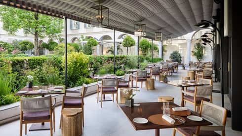 Covered terrace dining area lined with two rows of square tables looking out to verdant courtyard