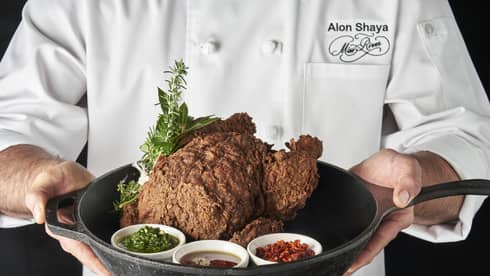 Person wearing a chef?s coat and holding a pan with a cooked turkey in it.