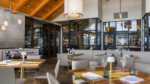 Restaurant with square wooden tables, light grey chairs, and vaulted ceiling