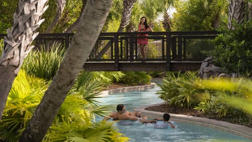 A woman watches from a bridge as a man and young boy float on inflatable tubes down the Lazy River at Four Seasons Orlando