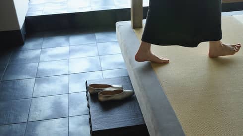Discarded shoes on step as person walks barefoot across mat-covered floor