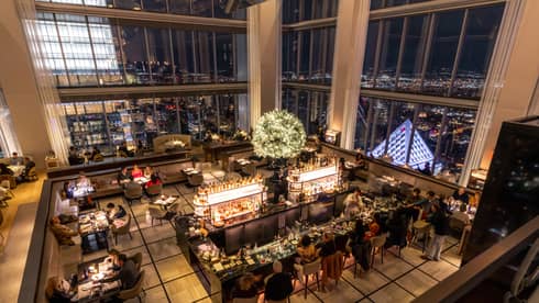 Aerial view of a dining room with floor-to-ceiling windows and a view of the city.