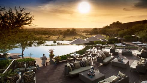 Server carries tray through Terrace Bar outdoor patio by lounge chairs, swimming pool at sunset