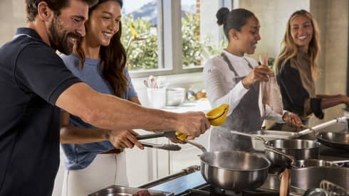 Four guests smiling while cooking in the kitchen.