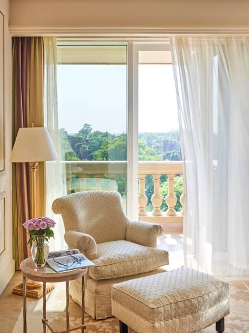 Beige and off white French-style chair with ottoman near window overlooking botanical gardens