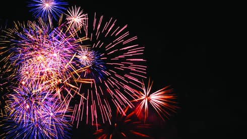 A clear night sky is filled with colorful fireworks of blue, red, and orange, holiday
