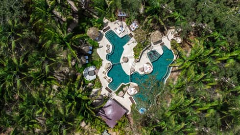 A bird's-eye view of an outdoor plunge pool in a luxury tent resort, surrounded by lush greenery