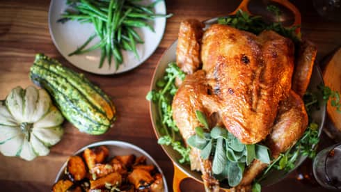 Roast turkey with fresh herbs on platter, presented on wood tabletop with gourds and green beans on white plate
