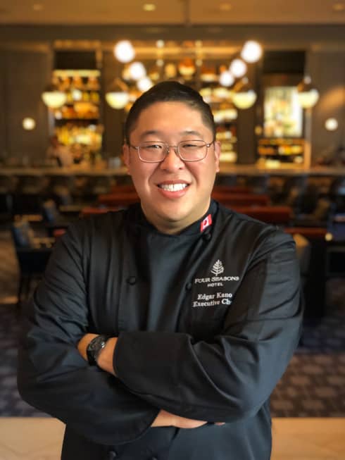 Headshot of Executive Chef Edgar Kano with dimly-lit restaurant in the background.