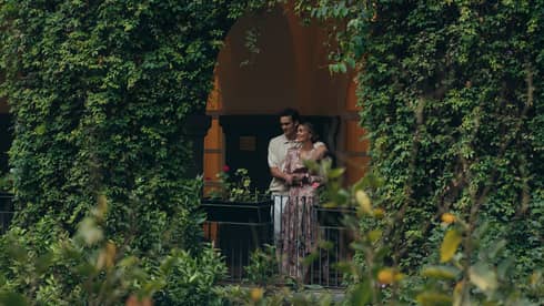 Couple standing on a balcony covered by lush greenery, enjoying a peaceful moment surrounded by nature in an intimate, serene garden setting.
