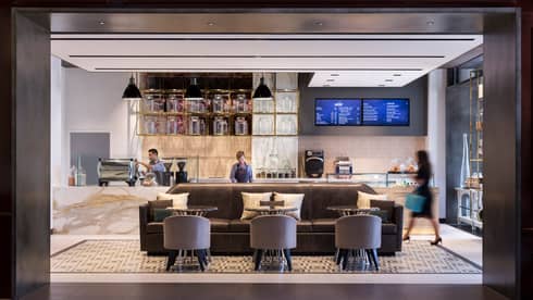 Three staff members at different stations in contemporary Stir lounge, brown sofa with three round tables and club chairs