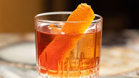 Drinking glass on a table with a large orange slice in it.