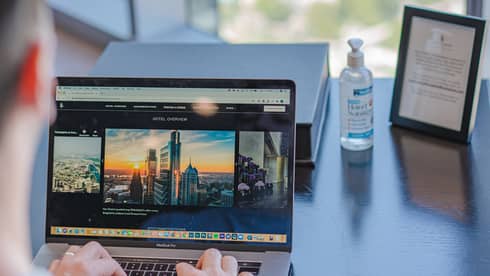 Man types on a laptop at desk, with city view blurred in the background