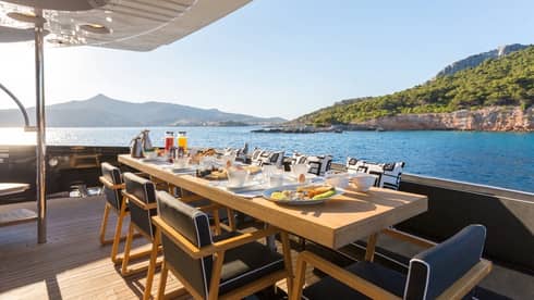 Dining setup on yacht deck overlooking blue water and lush landscape