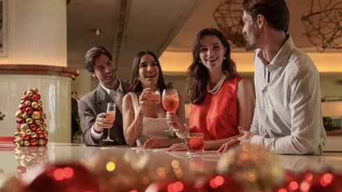 Group of four dressed in casual cocktail attire stand smiling at a white marble bar decorated with red and gold ornaments
