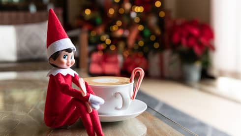 Elf on the Shelf sits next to a cappuccino