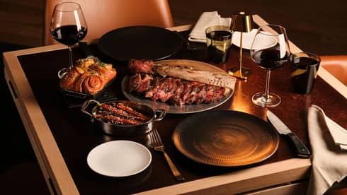 A dining table with wine glasses, culinary dishes and utensils beside plates