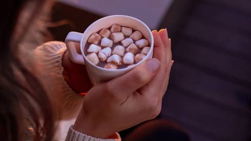 A woman holding hot chocolate by a fire.