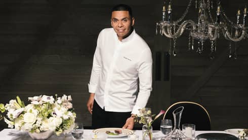 Chef Rogelio standing near a dining table with a bouquet of flowers on the table and place settings.