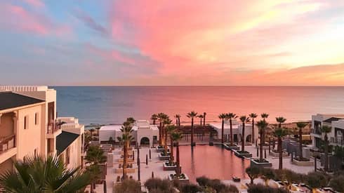 View over Four Seasons Hotel Tunis swimming pool, deck, palm trees by sea at sunset