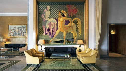 Almada Negreiros Lounge yellow armchairs below large handmade tapestry depicting centaurs