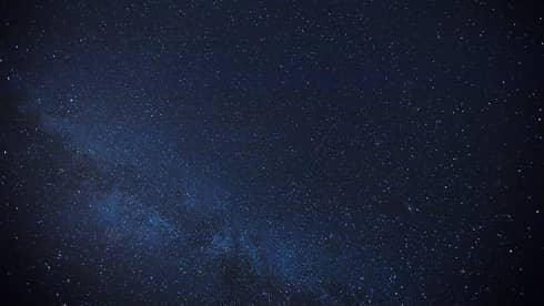 Thousands of stars dusting across a clear night sky; a cluster of stars form the Milky Way, just barely visible in the sky.