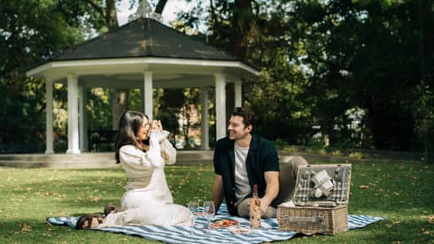 Two guests having a picnic outside surrounded by nature and sunlight through the trees