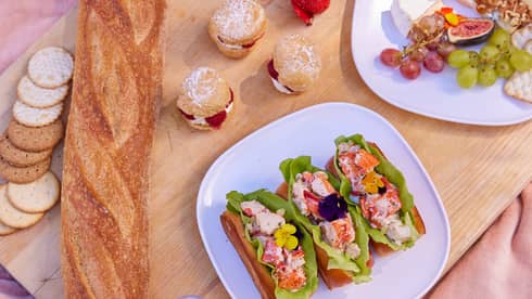 Plates of food and bowls of fruit on a picnic blanket