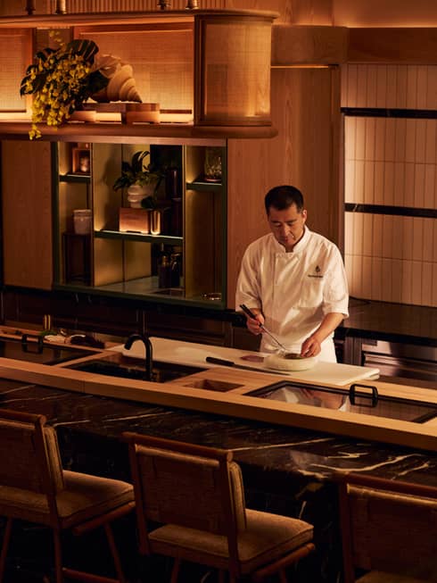 Chef in action at sushi counter in dimly lit, contemporary restaurant