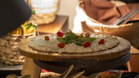 Cheese and za'atar manakeesh garnished with grape tomatoes and garnish on round cutting board