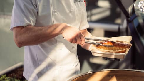 A chef using tongs to place food on a grill