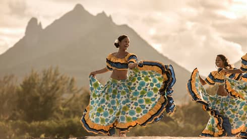 Zilwa Night Sega dancer twirls in colourful dress on sand in front of mountain, sunset