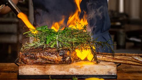 Chef wearing black apron and cooking meal using fire.