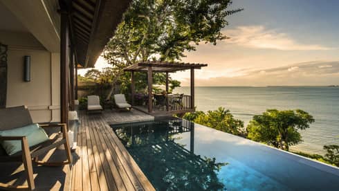 Private Ocean Villa patio at sunset with infinity swimming pool reflecting trees, clouds, white lounge chairs on side