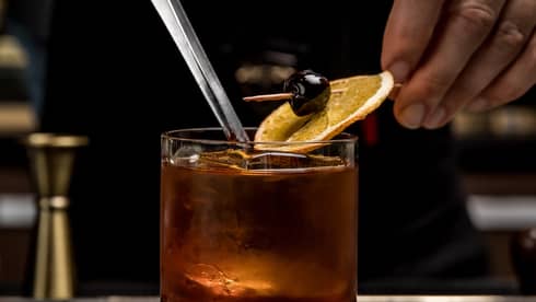 Close up of a bartender's hands gently placing an orange-and-cherry garnish on an Old Fashioned