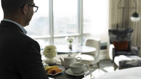 A man carries a tray of tea inside a hotel guest room with window