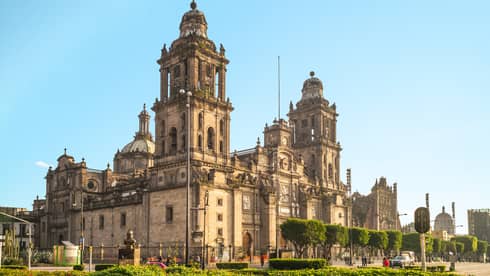 A large old building surrounded by streets and plants.