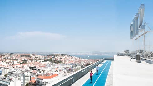 Aerial view of backs of man and woman running on blue rooftop outdoor track, Lisbon city roofs below