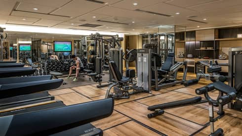 Man sits on bench, lifts weights on Fitness Centre by cardio machines 